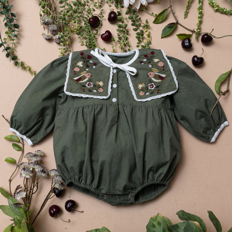 green sewn romper with embroidered collar on a beige background with plants and fruit