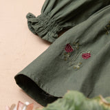 close up of green sewn dress with flower embroidery for kids