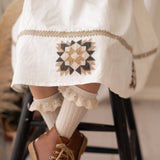 close up of a patchwork detail on a white dress worn by a girl in brown shoes