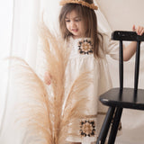 young girl wearing a white patchwork dress in a room