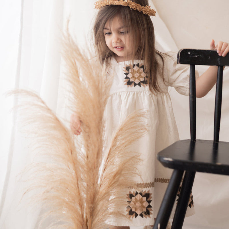 young girl wearing a white patchwork dress in a room