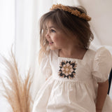 young girl wearing a white patchwork dress in a room