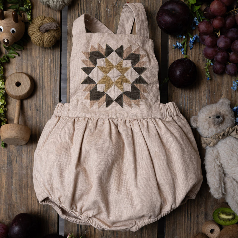 nude patchwork romper for kids on wooden background surrounded with fruit and toys