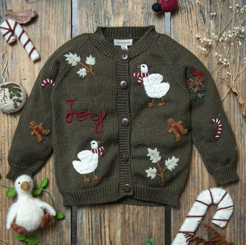 Joy Cardigan in pine green laid out on a wooden surface, set in a festive Christmas environment, highlighting the holiday motifs and the cozy, luxurious merino wool.