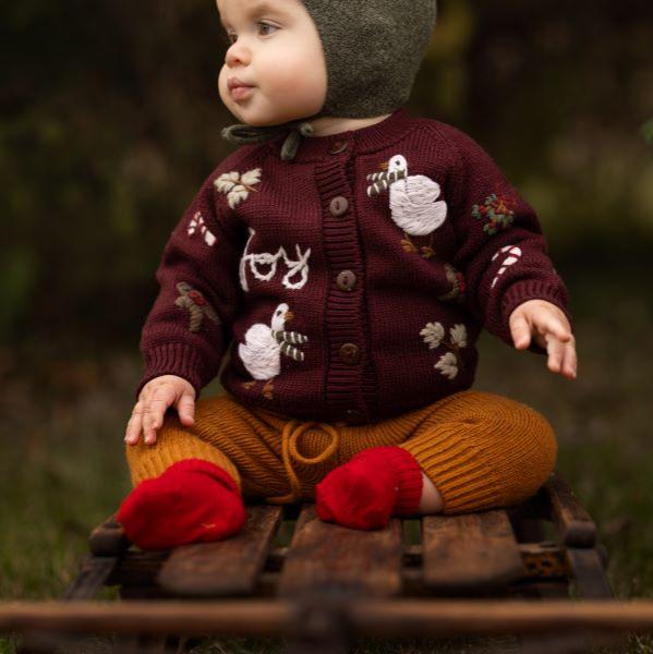 a baby wearing knitted and embroidered holiday goose cardigan for christmas in color grape