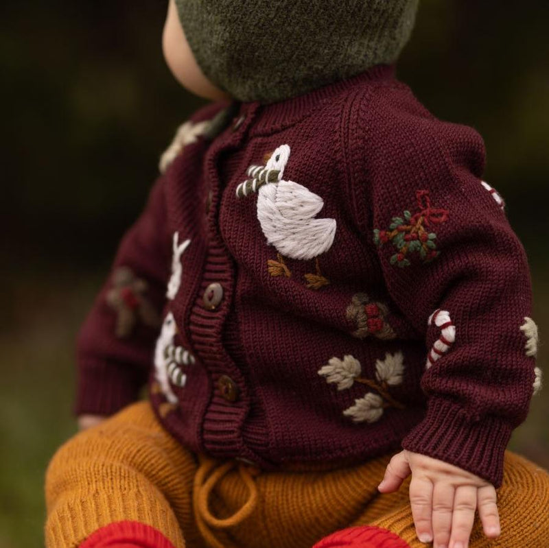 a baby wearing knitted and embroidered holiday goose cardigan for christmas in color grape