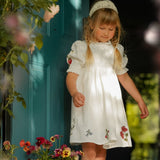 Young girl in a white dress with floral patterns standing in front of a teal door.