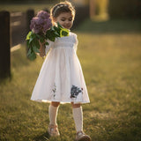 Little girl holding flowers while wearing a white embroidered dress outdoors