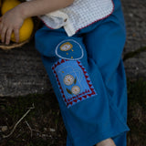 Boy wearing blue pants with embroidered design sitting on a stone surface.