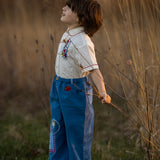 Child standing in a field holding a branch with a blurred natural background