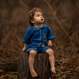 Child in a blue outfit sitting on a tree stump in a forest setting