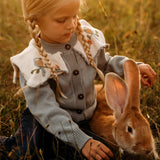 A little girl playing with an animal in a meadow, surrounded by greenery and nature, wearing the Little Birdie cardigan.







