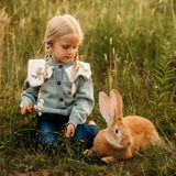 Girl in a field of flowers and greenery, with a bunny beside her, wearing the Little Birdie cardigan.







