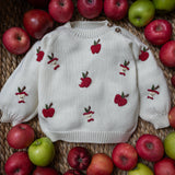 knitted and embroidered white apple sweater in a basket full of apples