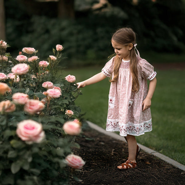 Young girl in a garden with pink flowers in a sewn dress