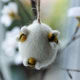 White felted owl ornament with yellow eyes hanging on a branch.
