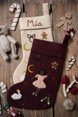 Two handcrafted Ballerina holiday stockings, including a dark grape one, displayed among various Christmas decorations, highlighting their intricate embroidery and festive appeal.