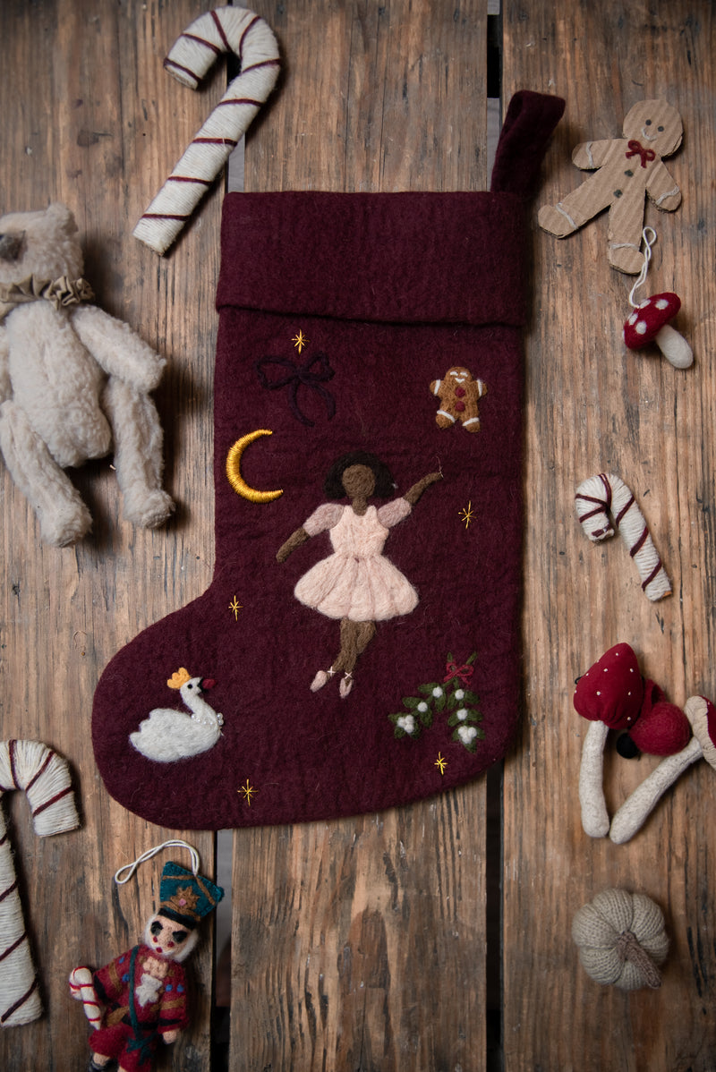 Dark grape holiday stocking featuring an embroidered ballerina, positioned among other Christmas decorations, showcasing its detailed design and 100% wool material.