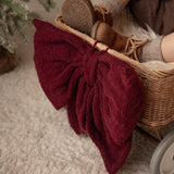 Child's feet in brown boots with a red knitted bow on a beige surface, next to a small wicker basket.
