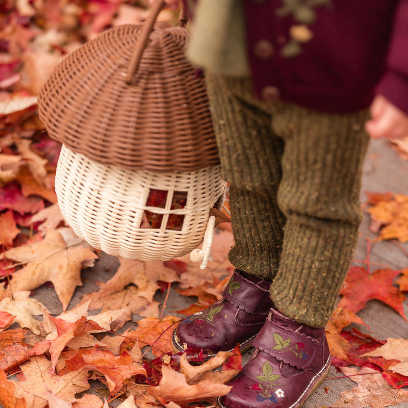 Close-up of moss rib leggings paired with plum knitwear and tiny purple shoes among autumn leaves.

