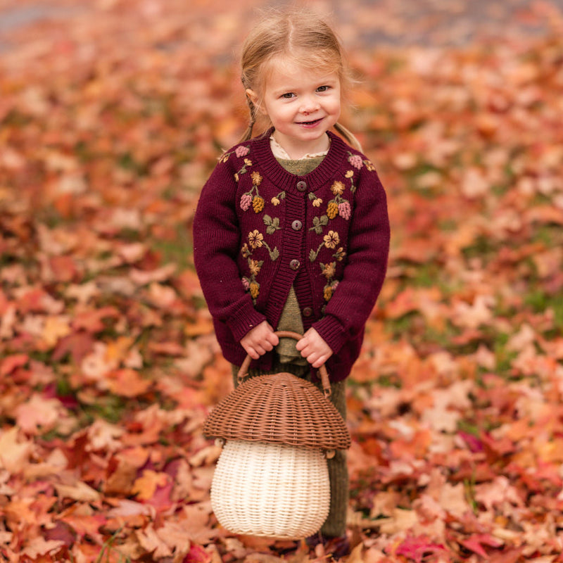 Young girl in a floral cardigan standing in a field of autumn leaves holding a lantern.