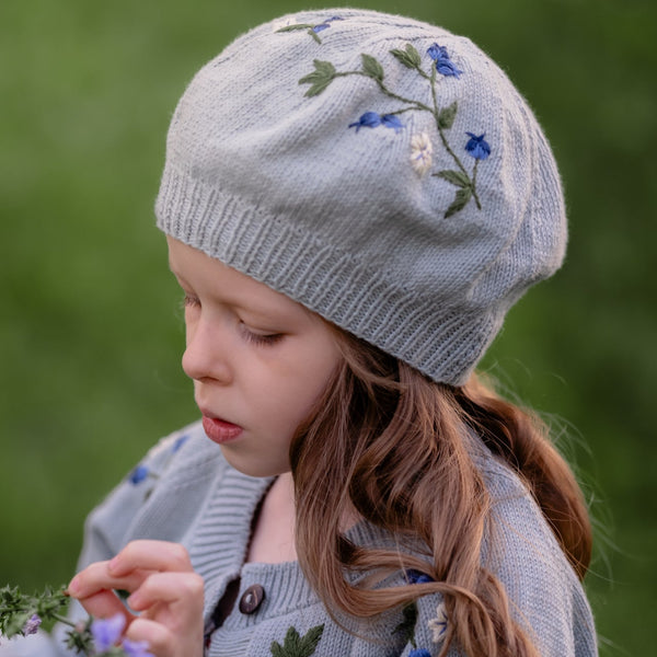 Child wearing a light blue knitted hat and cardigan with blueberries patterns outdoors.