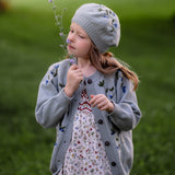Young girl in a gray cardigan and floral dress holding a flower in a grassy field
