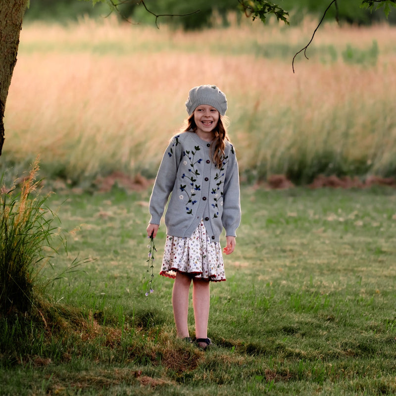 Young girl standing in a field wearing a blue sweater and dress
