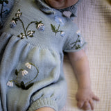Baby wearing a light blue embroidered romper on a textured surface