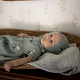 Baby in a floral outfit lying on a bed with a mirror and floral wallpaper in the background
