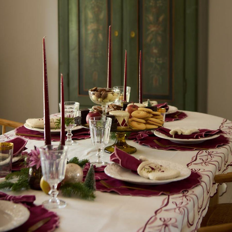 Cream white Bow Heirloom tablecloth elegantly draped over a dining table setting, featuring the intricate bow print and scalloped edges, enhancing the festive and sophisticated ambiance of the holiday arrangement.