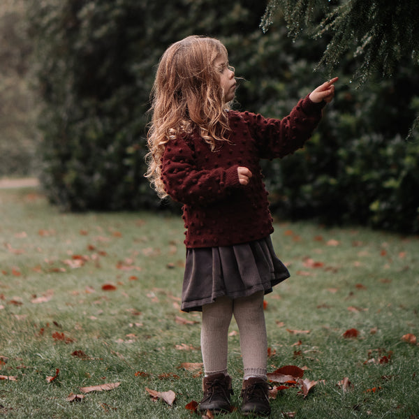 Child in a red sweater and skirt standing in a grassy area with trees in the background