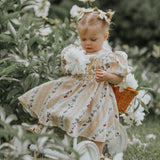 Little girl wearing the Bunny Breeze dress in apricot, playing outdoors with a natural backdrop, showcasing the playful bunny and floral print.







