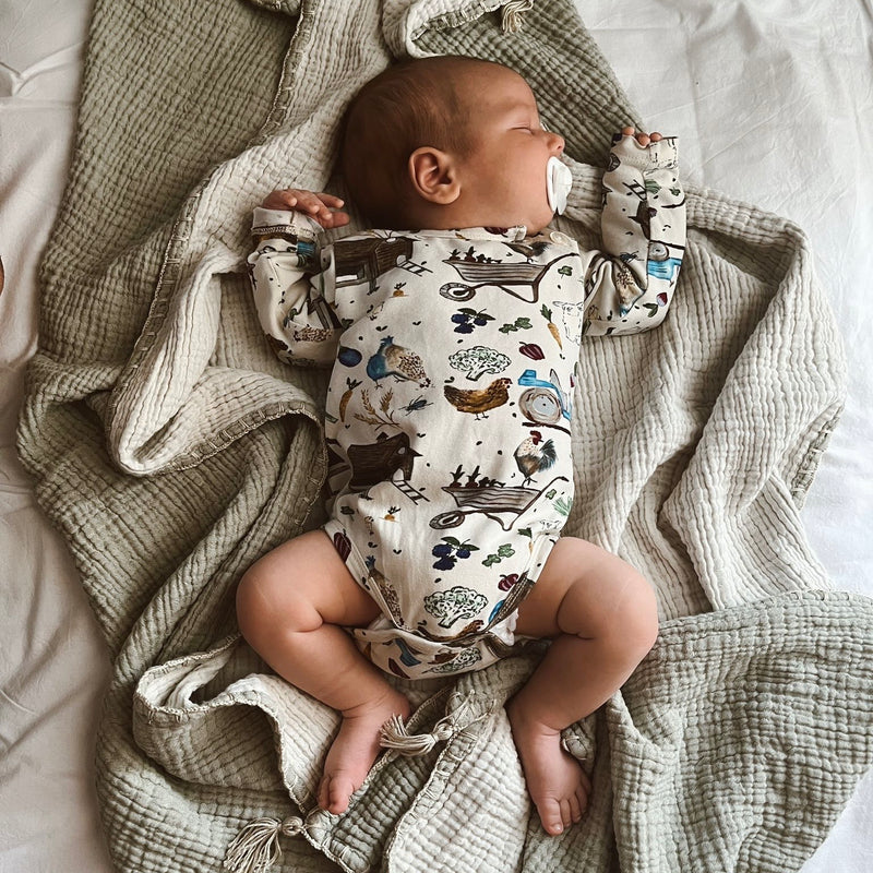 Baby lying down wearing a soft cotton jersey Little Farm Onesie in cream, featuring adorable farm motifs and snap buttons for easy diaper change.







