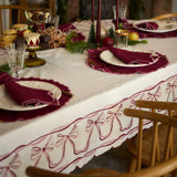 Bow Heirloom tablecloth in cream white draped over a dining table, demonstrating its graceful bow print and sophisticated scalloped edges in a festive holiday setting.
