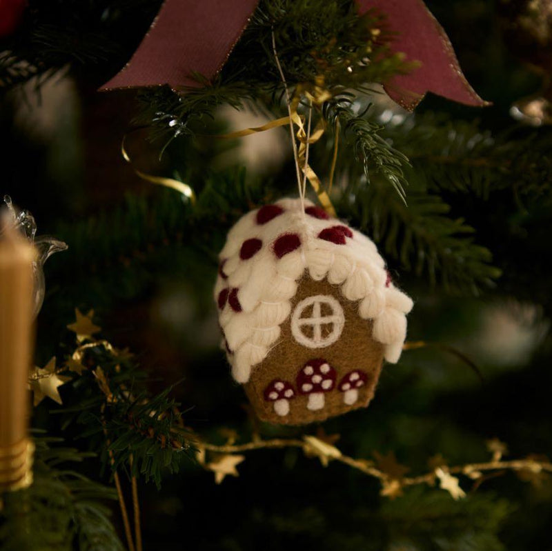 Handcrafted gingerbread house ornament with a whimsical mushroom detail, displayed on a Christmas tree surrounded by other festive decorations. The ornament features intricate embroidery and punch needle accents, adding a charming touch to the holiday scene.