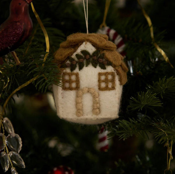 Handcrafted gingerbread house ornament in white, hanging on a Christmas tree. The ornament features intricate details and festive charm, crafted from 100% wool, adding a touch of traditional warmth to the holiday decor.