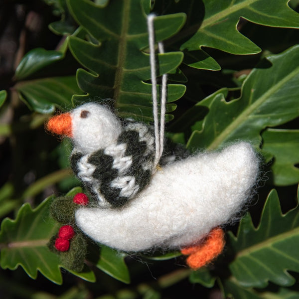 Handcrafted felted goose ornament wearing a cozy scarf, gracefully hanging from a branch of a Christmas tree.