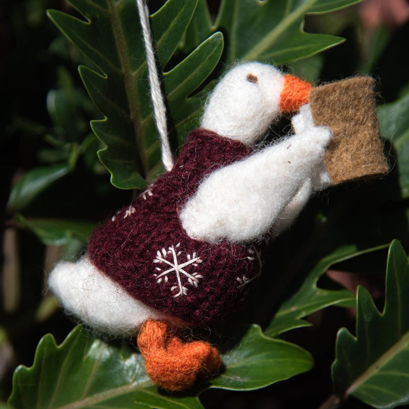 Felted goose ornament with red vest as part of holiday decor, adding character to festive display.