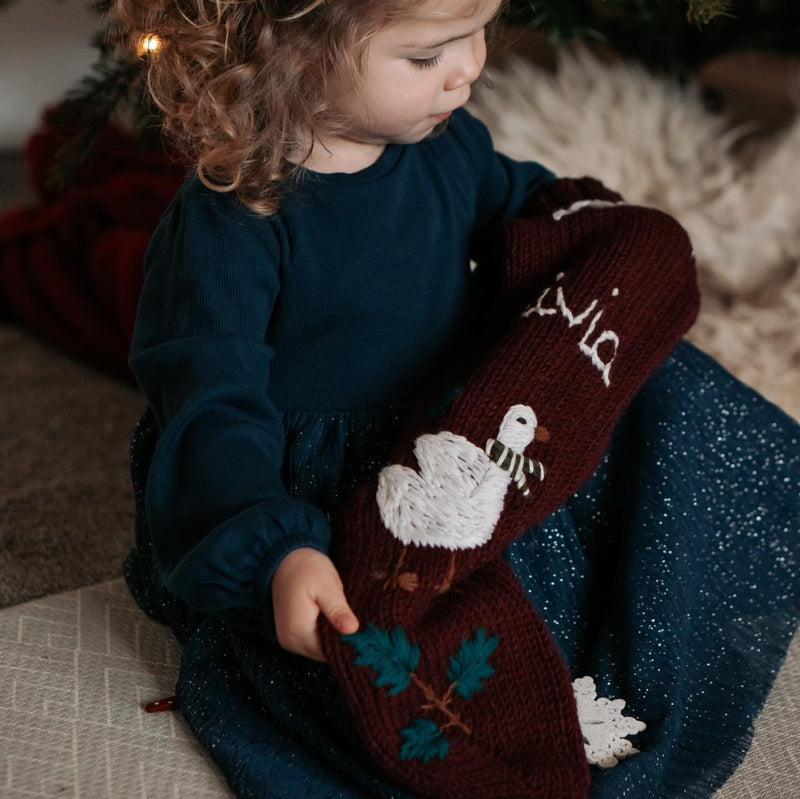 girl holding knitted and embroidered goose stocking with personalized name