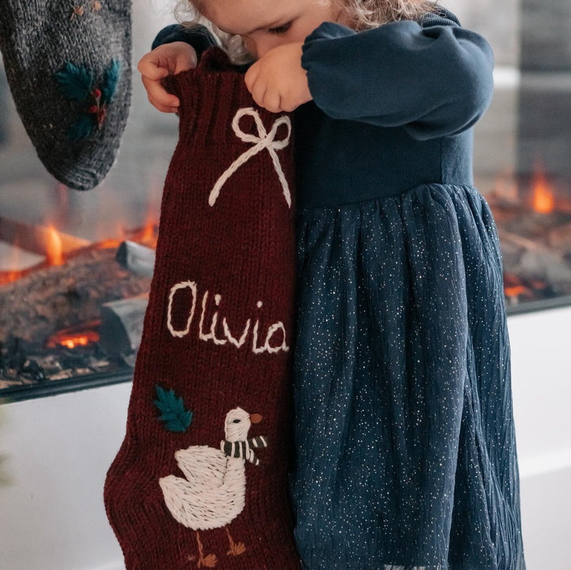 girl holding knitted and embroidered goose stocking with personalized name