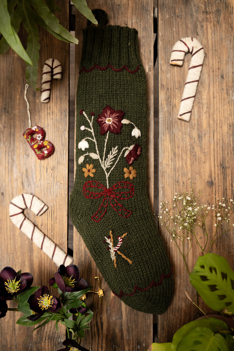 Knitted green Christmas stocking with floral and candy cane designs on a wooden background.