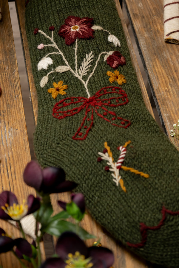 Green knitted stocking with floral embroidery on a wooden surface