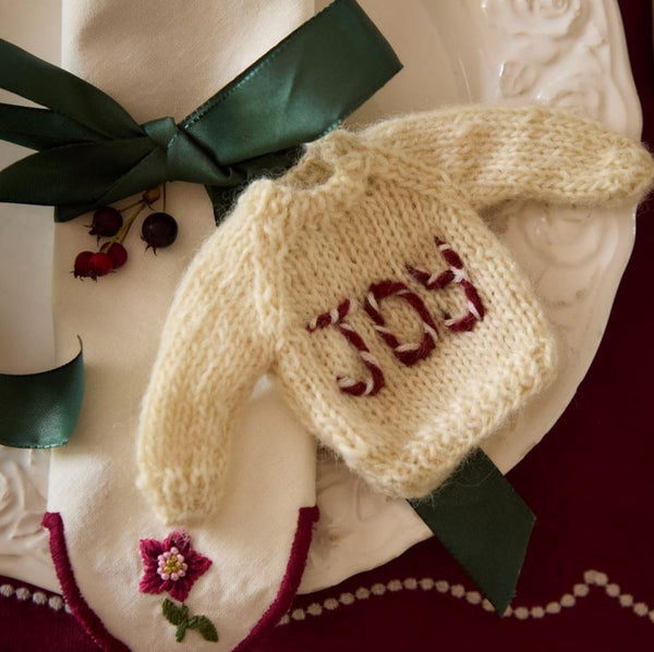 Sweater ornament with 'JOY' embroidery used in table setting, enhancing the festive atmosphere of holiday gatherings.