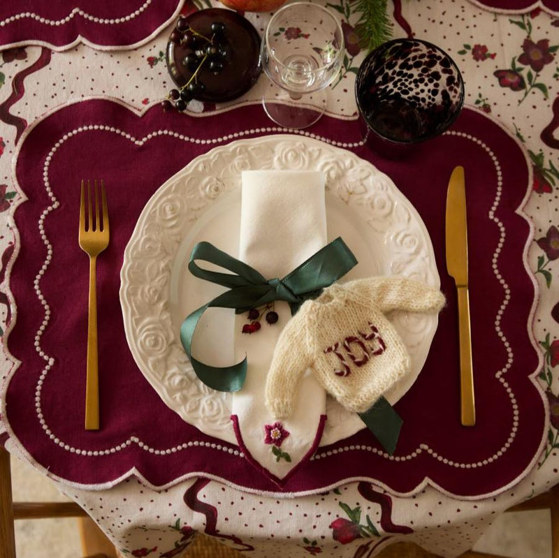 Sweater ornament with 'JOY' embroidery displayed on a festive napkin, adding a cheerful touch to the holiday table decor.