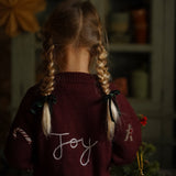 Child wearing a sweater with 'Joy' on it in a cozy indoor setting.