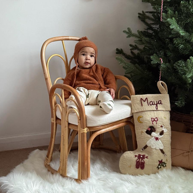 a little baby sitting next to a christmas tree with a personalized felted odette stocking