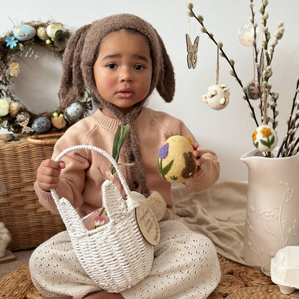 A child holding the Artisan Easter Egg Bunny Butt in the left hand, with a basket in the right hand, surrounded by festive decorations.

