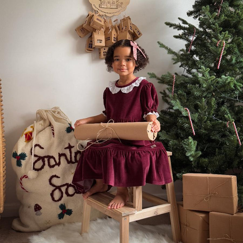 a girl sitting next to a christmas tree with a santa sack next to it