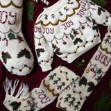 Joy Scarf in Cream White displayed with a coordinating knitted Joy sweater in Cream White and Christmas stocking with hand-embroidered holiday motifs, creating a beautifully coordinated festive display.
